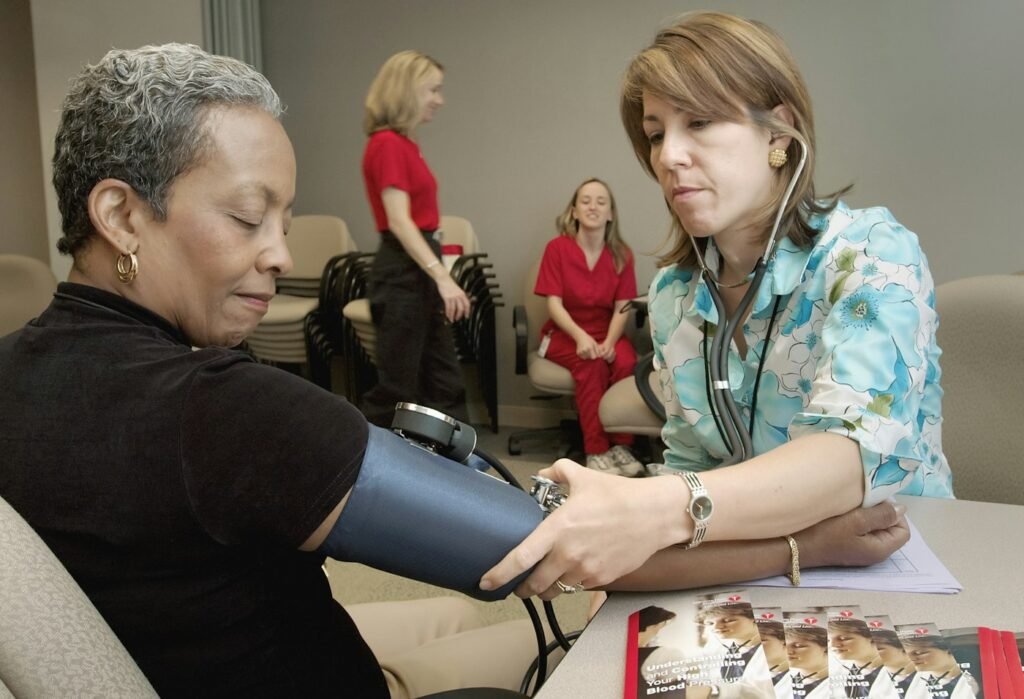 A clinician checks a patient's blood pressure in a waiting room with other patients nearby