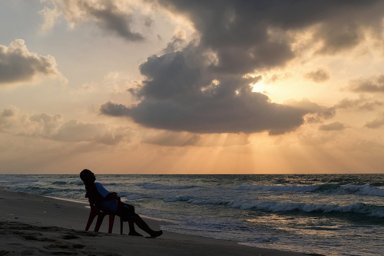 Person resting in a chair on the beach at sunset
