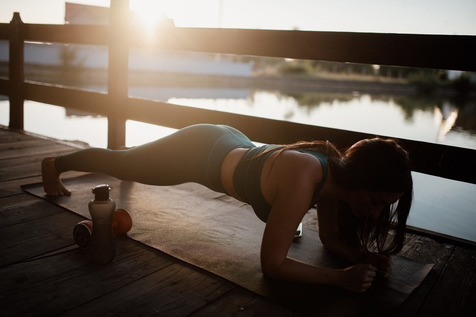 Woman holding a plank on an exercise mat with dumbbells nearby