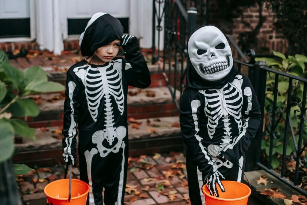 Two children in skeleton Halloween costumes carrying trick-or-treat buckets