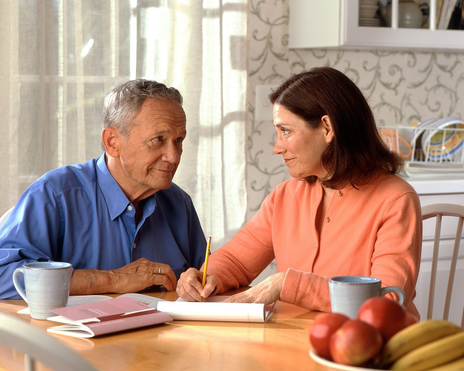 Two adults sitting at a kitchen table with coffee, making a written plan together