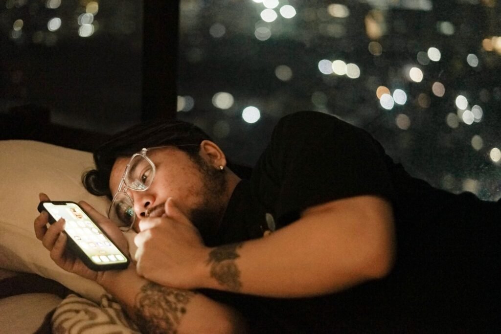 Man lying in bed scrolling his phone late at night in a dark room